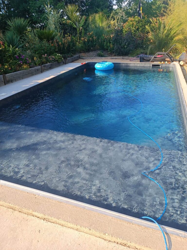 Piscine liner foncé : la beauté d'une plage immergée au jardin. Grande piscine rectangulaire au liner sombre, avec une large plage immergée. L'eau bleu profond est entourée d'un jardin luxuriant et tropical.