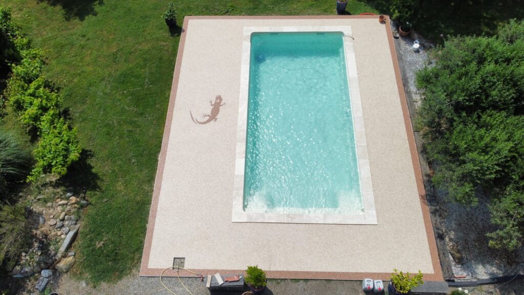 Piscine moderne : Terrasse en résine décorative avec lézard Piscine extérieure et terrasse rectangulaire en agrégats de résine beige. La margelle est en pierre claire, avec un grand lézard décoratif.