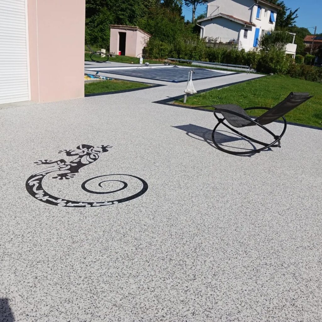 Résine drainante terrasse : motif lézard pour plage piscine. Terrasse en résine drainante claire avec incrustation d'un grand lézard noir. Plage de piscine et chaise longue moderne.