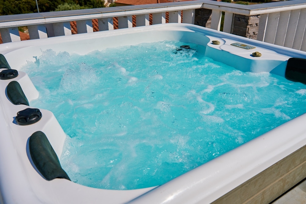 Spa extérieur : Profitez d'un jacuzzi bouillonnant sur terrasse. Bain à remous extérieur sur terrasse, rempli d'eau turquoise bouillonnante. Coque blanche et appuie-têtes sombres.