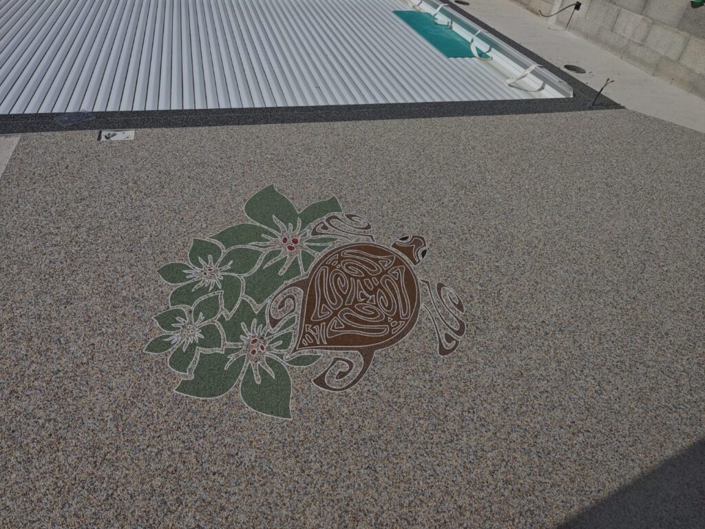 Tortue Honu tribale : Motif en agrégats pour terrasse. Honu, tortue marine stylisée avec motifs tribaux, entourée de fleurs vertes, sur un revêtement de sol en agrégats beige.